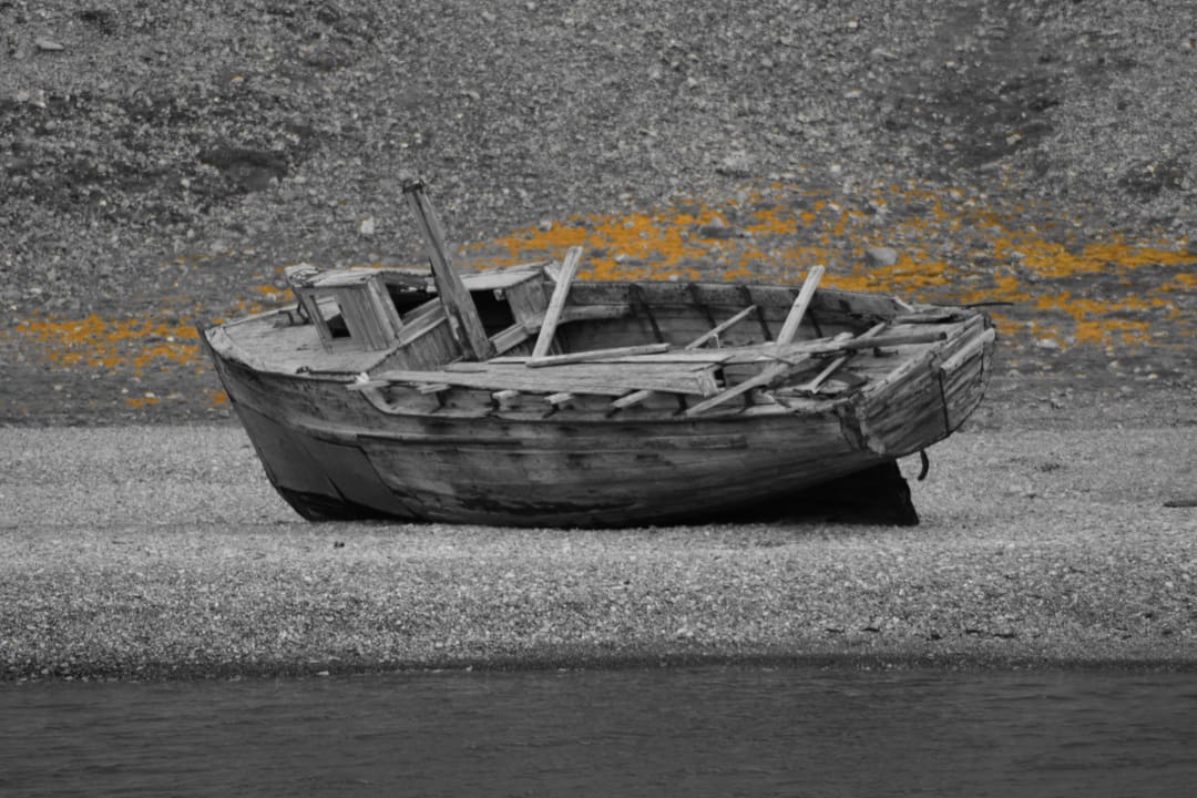 Weathered wooden rowboat abandoned on an Arctic gravel shore, faded paint, Svalbard Norway