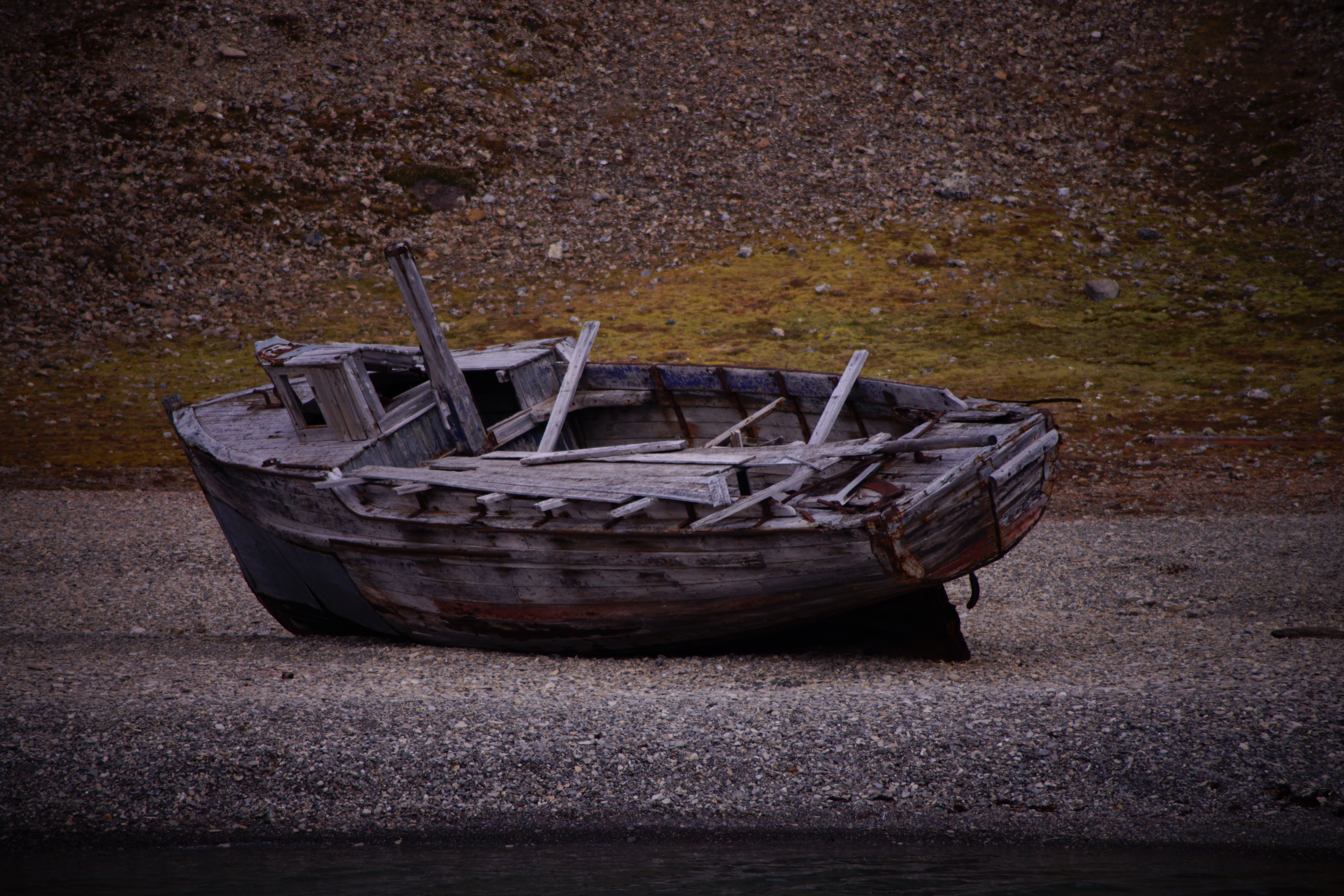 Weathered wooden rowboat abandoned on an Arctic gravel shore, faded paint, Svalbard Norway