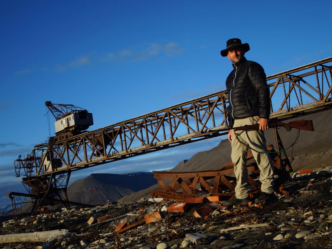 Ralf, urban exploration photographer, standing at an abandoned Soviet-era industrial crane structure in Pyramiden, Svalbard, Norway